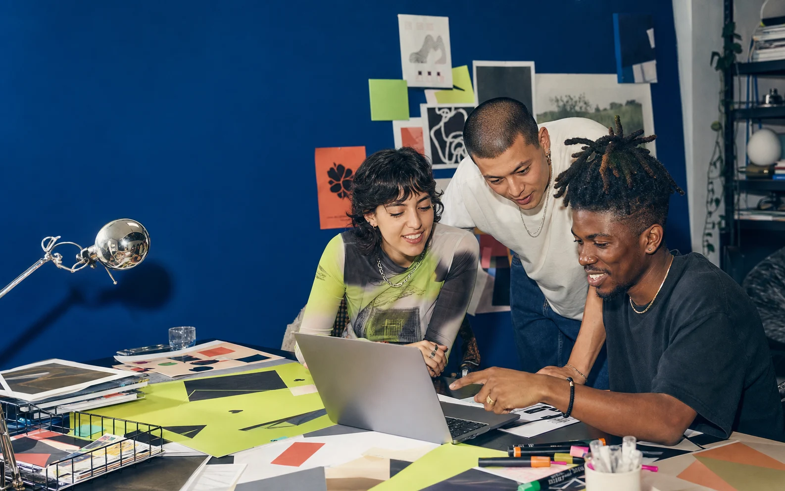 Three young creatives collaborating around a laptop in a colorful studio